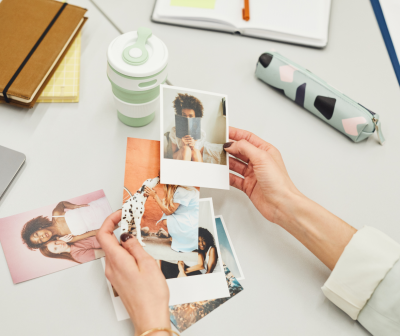 Mesa branca com livros, copo, estojo e fotografias coloridas