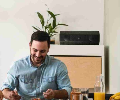 Pessoa sorridente a comer numa mesa com sumo, frutas e fundos neutros.