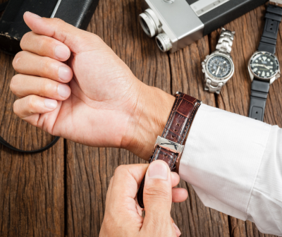 Pulseira de relógio castanha de couro com padrão crocodilo e fivela prateada num pulso com camisa branca