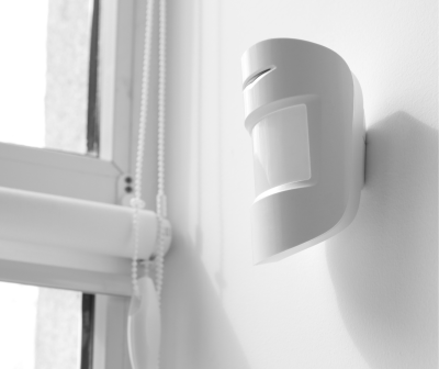 Sensor de movimento branco junto a janela branca com cortina de corda