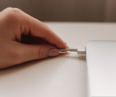 Mão segurando cabo branco ligado a dispositivo prateado sobre superfície branca