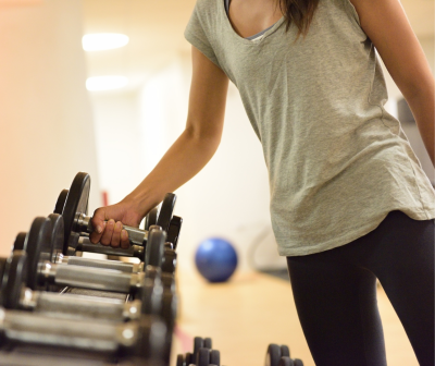 Pessoa a segurar haltere em ginásio com t-shirt cinza e leggings pretas