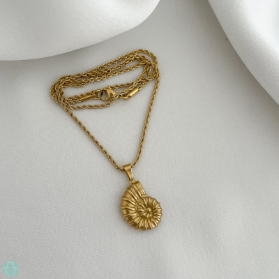 Colar dourado com pingente de concha espiral sobre tecido branco