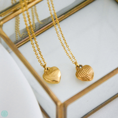 Dois colares dourados com pendentes em forma de coração sobre caixa transparente