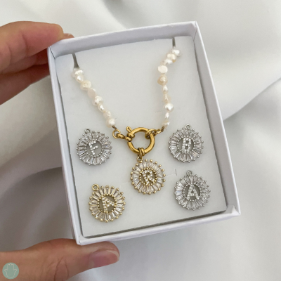 Colar de pérolas com pingentes de letras dourados e prateados numa caixa branca