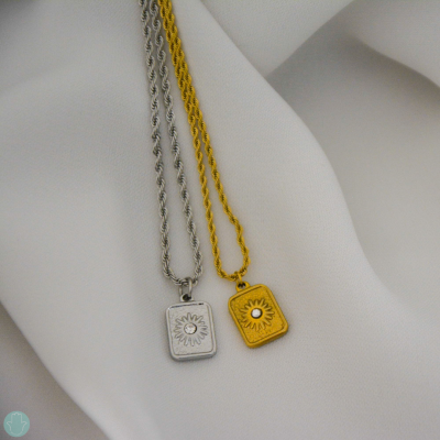 Dois colares com pendentes retangulares, um prateado e outro dourado, sobre tecido branco