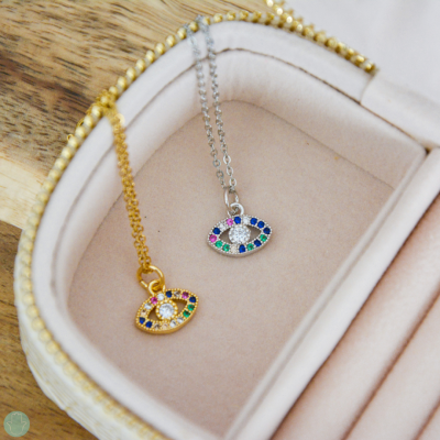 Colares com pendentes de olho em ouro e prata numa caixa de joias bege