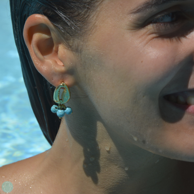 Brinco com concha e contas azuis usado por mulher junto a piscina