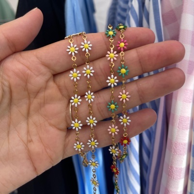 Pulseiras douradas com flores esmaltadas coloridas seguradas por uma mão