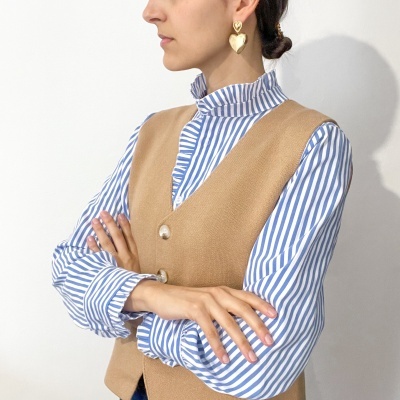 Colete bege com camisa listrada azul e branca e brincos de coração dourados