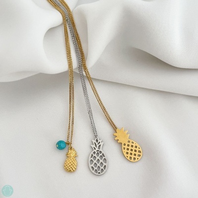 Três colares com pendentes de abacaxi em dourado e prateado sobre tecido branco