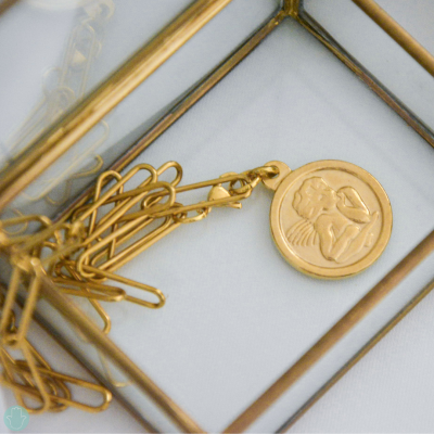 Clips de papel dourados com medalhão dourado de anjo dentro de uma moldura dourada.