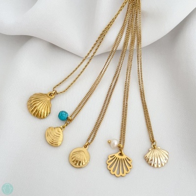 Cinco colares dourados com pendentes em forma de concha sobre tecido branco