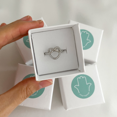 Anel de nó em forma de coração em caixa branca junto a outras caixas semelhantes.