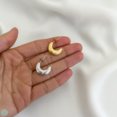 Par de brincos semi-aro dourado e prateado com textura, na mão
