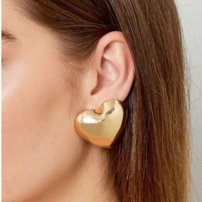 Brinco dourado em forma de coração na orelha de mulher