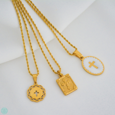 Três colares dourados com diferentes pendentes religiosos sobre tecido branco