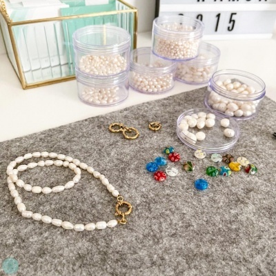 Colar de pérolas brancas, caixas com pérolas e contas coloridas sobre superfície cinzenta