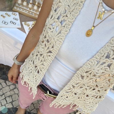 Colete crochet bege, t-shirt branca, calças rosa, colares dourados, banca de feira com anéis