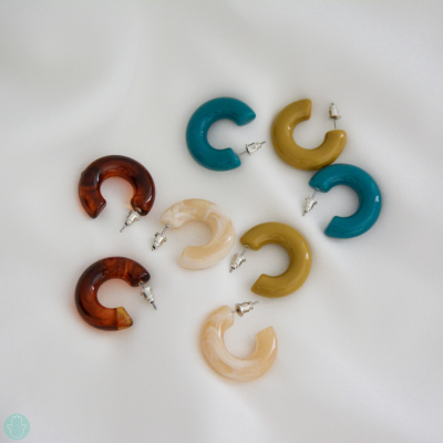 Brincos de argola em acrílico com várias cores e textura marmoreada sobre tecido branco