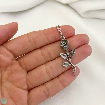 Colar prateado com pendente de rosa em mão sobre tecido branco