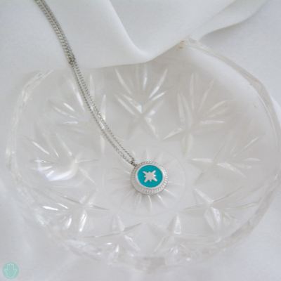 Colar com pendente azul e branco colocado numa tigela de vidro transparente com padrão gravado