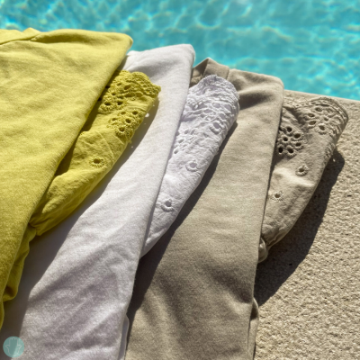 Peças de roupa dobradas com bordados em várias cores ao lado de piscina