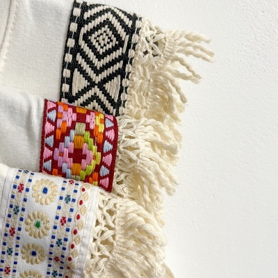 Três tecidos brancos com franjas e bordados coloridos e preto e branco