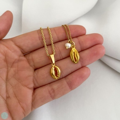 Colares dourados com pendentes de búzio e pérola numa mão