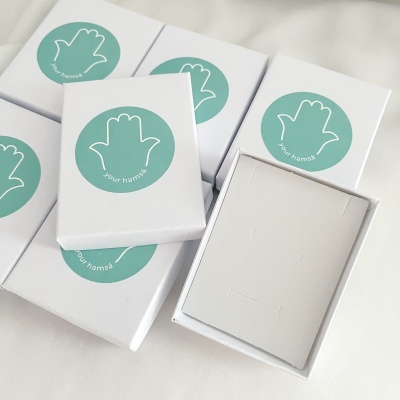 Caixas brancas com selo verde de mão e texto 'your hamsa'