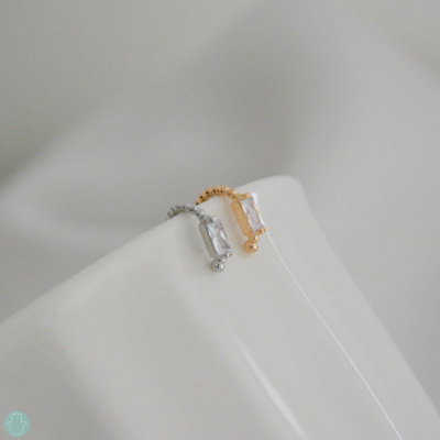 Brincos pequenos prateado e dourado com pedra retangular em superfície branca