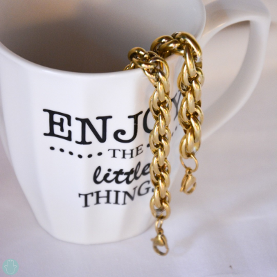 Caneca branca com frase preta e pulseiras douradas penduradas na alça