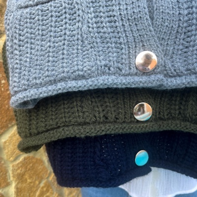 Três peças de malha azul claro, verde escuro e azul escuro dobradas com botões prateados