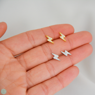 Brincos pequenos em forma de raio dourados e prateados com pedras brilhantes na mão
