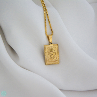 Colar dourado com pendente retangular em metal com relevo e textos sobre tecido branco