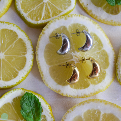 Brincos em forma de meia-lua prateados e dourados sobre fatias de limão e folhas de hortelã