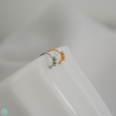 Dois anéis, um dourado e outro prateado, com pérolas, sobre superfície branca