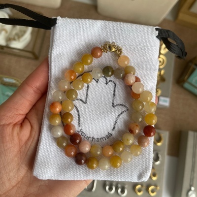 Pulseira de contas coloridas sobre bolsa branca com desenho de mão.