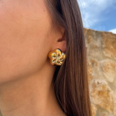 Brinco dourado em forma de flor usado na orelha de uma pessoa