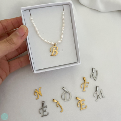 Colar com pingente letra B e outros pingentes em letras douradas e prateadas numa caixa branca