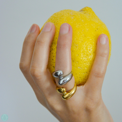 Mão com anéis dourado e prateado segurando limão amarelo