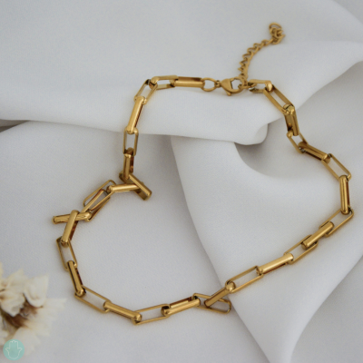 Colar dourado composto por elos retangulares sobre tecido branco