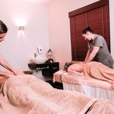 Sala de massagens com duas pessoas a receber tratamentos em macas cobertas com toalhas cor de salmão.