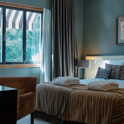 Quarto com cama de casal, cortinas e cadeira castanha.