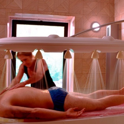 Mesa de massagens com homem deitado e massagista aplicando massagem sob jatos de água