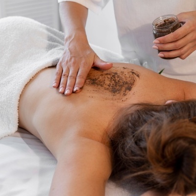 Pessoa a receber esfoliação corporal nas costas com esfoliante marrom em ambiente de massagem
