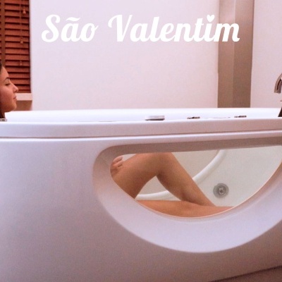 Banheira branca oval moderna com janela transparente lateral e mulher relaxando dentro.