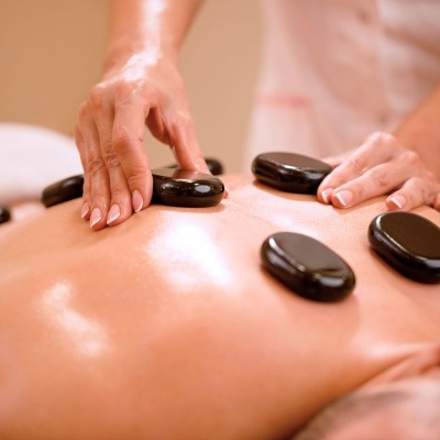 Massagem com pedras quentes e mãos femininas aplicando pedras pretas nas costas