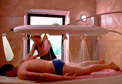 Mesa de massagens com homem deitado e massagista aplicando massagem sob jatos de água