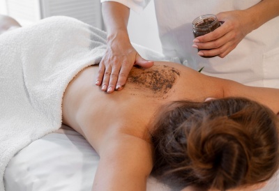 Pessoa a receber esfoliação corporal nas costas com esfoliante marrom em ambiente de massagem